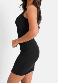 Robe noire ajustée sans manches, texture côtelée, longueur genou. Style simple avec des accents minimalistes et une silhouette lisse.