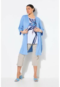 Hellblaues offenes Strickjacke, weißes Oberteil mit blauem Blumenmuster, beiges kurzes Hosen, und passende blaue High-Heels.