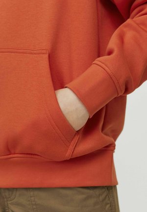 Orange sweatshirt med en frontlomme og ribbet manchetter. Stoffet ser blødt ud, med synlige syninger.