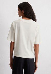 T-shirt a maniche corte in cotone avorio con una vestibilità rilassata, cuciture visibili e scollo rotondo, abbinato a pantaloni neri larghi.