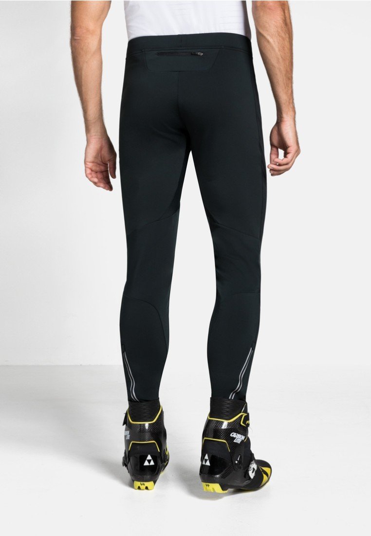 Eng anliegende schwarze Leggings mit einer glatten Textur, ausgestattet mit reflektierenden Akzenten und einer Reißverschlusstasche auf der Rückseite, kombiniert mit schwarzen und gelben Schuhen.