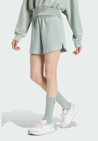 Mint green athletic shorts with elastic waistband, side slits, paired with matching ribbed socks and white sneakers. Smooth fabric texture.