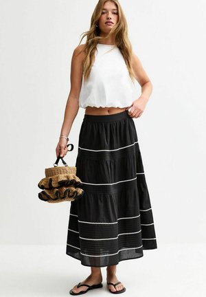 Falda negra de volantes con acentos blancos, combinada con una parte superior blanca corta. Los accesorios incluyen un bolso de mimbre con bordes rizados y sandalias de dedo.