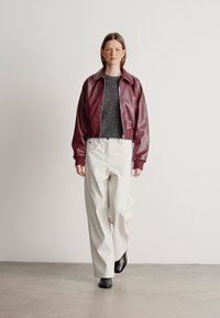 Μπορντό δερμάτινο μπουφάν, γκρίζος υφασμάτινος πουλόβερ, λευκά παντελόνια με φαρδιά καβάνα, μαύρες μπότες μέχρι τον αστράγαλο, μινιμαλιστικός σχεδιασμός, μαλλιά σε μεσαίο μήκος και ίσια.