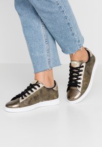 Sneakers w kamuflażowym wzorze z metalicznymi złotymi akcentami, czarnymi sznurówkami i białą podeszwą; materiał o fakturze oraz kontrastowy panel z zamszu.