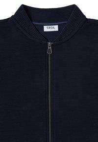 Giacca zip-up blu navy con texture rigata, colletto alto e zip metallica. Presenta un'etichetta "CECIL" all'interno del colletto.