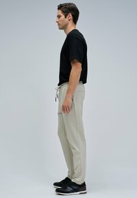 T-shirt en coton noir, pantalon beige à cordon de serrage et baskets noires. Vue de côté, mettant en avant la coupe décontractée et la tenue décontractée. Texture lisse.