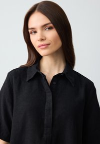 Czarna lniana koszula z kołnierzykiem, zapięciem na guziki, krótkimi rękawami i fakturowaną powierzchnią. Prosty design bez dodatkowych akcentów.