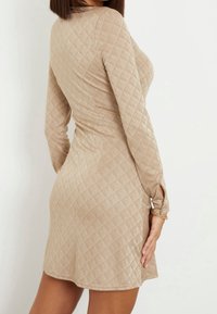 Long-sleeve, textured dress in beige with a diamond pattern, fitted silhouette, and button accents on sleeves. Soft, stretchy material.