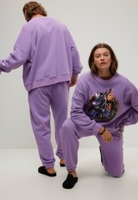 Paarse sweatshirt en joggingsbroek set, met een grafische print aan de voorkant. Zacht materiaal met een ontspannen pasvorm en geribbelde manchetten.
