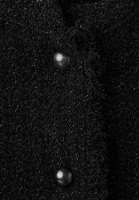 Czarna teksturowana tkanina z metalowymi guzikami, posiadająca postrzępione krawędzie, ukazująca miękką i lekko błyszczącą powierzchnię.