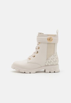 Stivali ankle beige con una finitura liscia, occhielli dorati e un polsino in tessuto rigato. Presentano un logo patternato sul lato e una suola spessa.