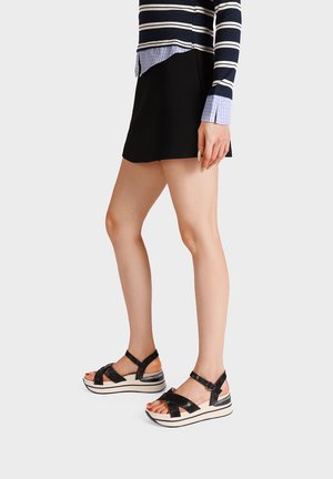 Donna che indossa sandali platform neri con cinturini alla caviglia, una minigonna nera e una maglia a maniche lunghe a righe blu navy e bianche.