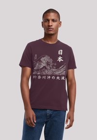 Maroon cotton t-shirt featuring a white graphic of waves and Japanese text, short sleeves, and a classic fit, worn by a model.