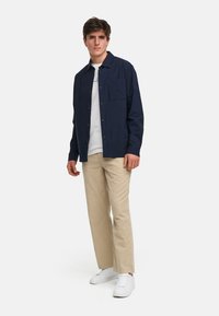 Marinblå skjorta med knappar, lättviktig tyg, avslappnad passform, en bröstficka. Matchad med beiga byxor och vita sneakers.