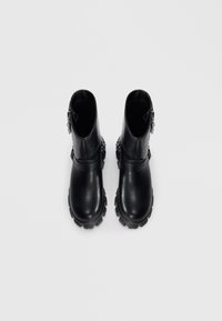 Botas de cuero negro hasta el tobillo con una suela de goma gruesa, que cuentan con un cierre lateral y un acento de correa decorativa. Acabado suave y puntera redondeada.
