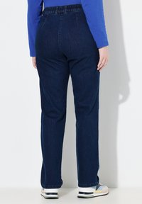 Ciemnoniebieskie jeansy z elastycznym pasem, prostymi nogawkami i delikatną fakturą; noszone z białymi i szarymi butami sportowymi.