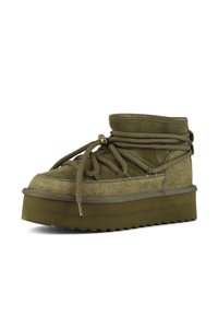Botín de ante verde oliva hasta el tobillo con punta redonda, suela gruesa texturizada y un sistema de cordones prominente. Presenta un cuello acolchado y un borde de suela en zigzag.
