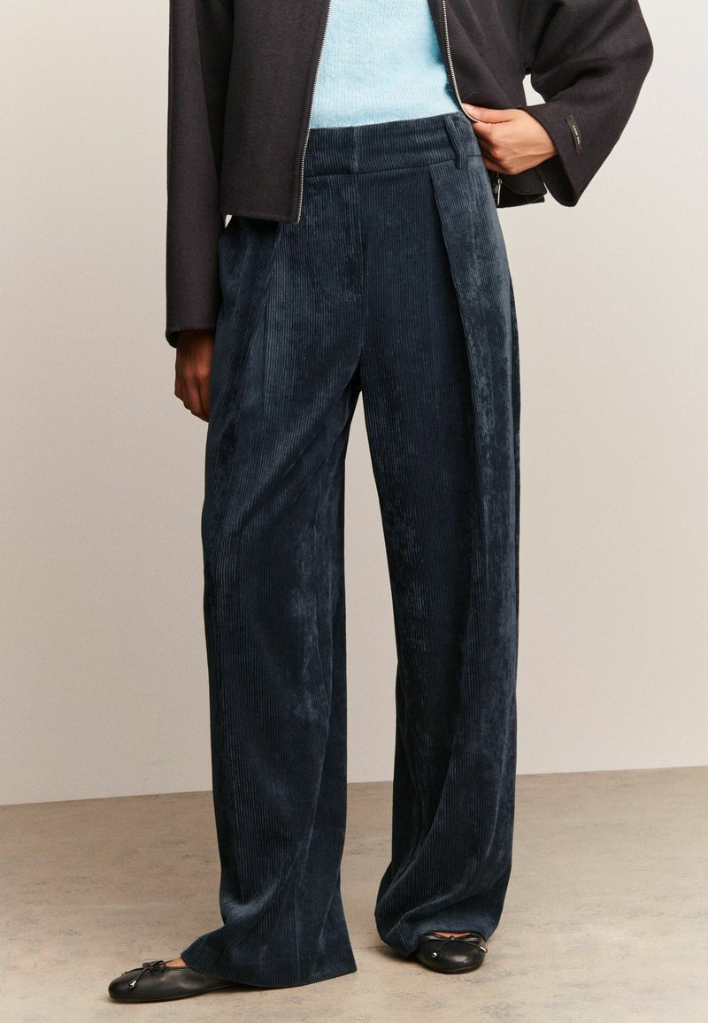 Pantalons larges en velours côtelé marine foncé, présentant une surface texturée, des plis à l'avant et une coupe décontractée.