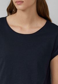 Ciemnoniebieska koszulka z okrągłym dekoltem, krótkimi rękawami i gładką fakturą. Posiada przeszycia wokół dekoltu.