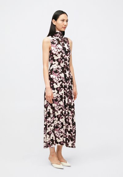 Αμάνικο φόρεμα με ψηλό λαιμό σε μαύρο και λευκό με ροζ λουλουδάτο σχέδιο. Λείο ύφασμα, μήκος μέχρι το πάτωμα με ροή στο σχέδιο. Φορώντας με μυτερές λευκές παντόφλες.