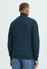 Mørkeblå høyhalset genser med en strukturert finish, ribbede mansjetter og kant, samt en klassisk passform, brukt med lyseblå jeans.