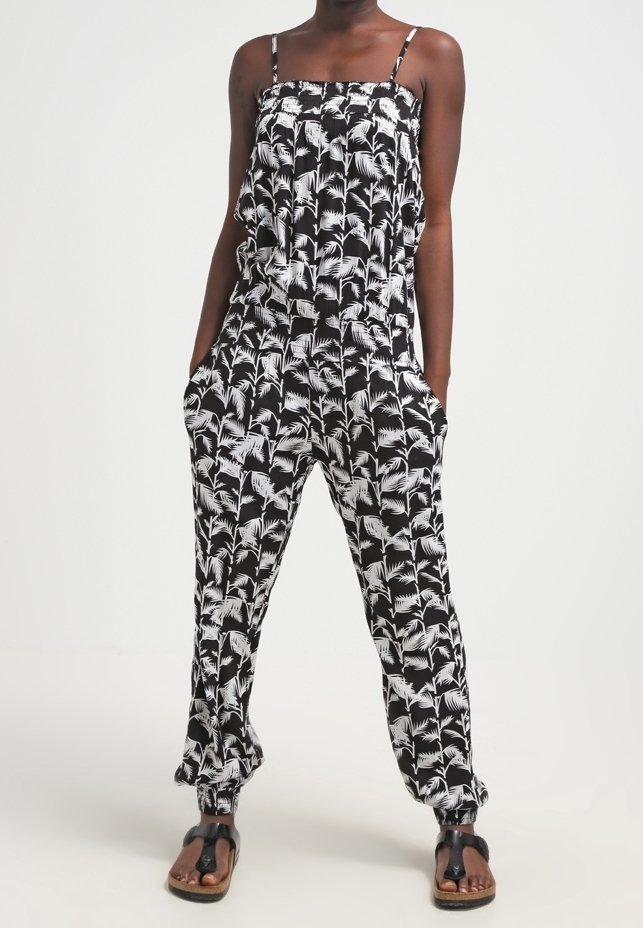 Svart jumpsuit med vitt palmbladsmönster, justerbara axelband, lös passform, fickor och elastiska ärmslut. Bärs med platta sandaler.
