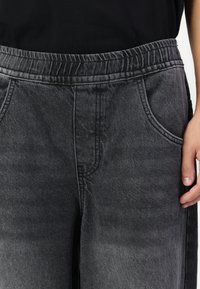 Black denim trousers featuring an elastic waistband, side pockets, and a faded texture with subtle stitching details.