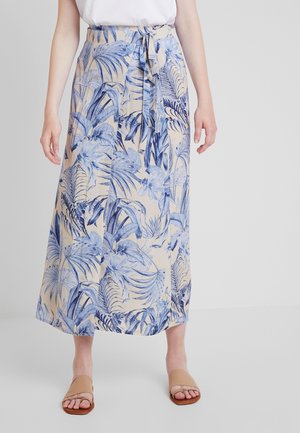 Maxi rok in een lichtbeige stof met blauwe tropische bladeren. Heeft een strikband in de taille en een losse, vloeiende silhoutte. Gecombineerd met platte sandalen.