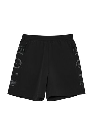 Mand stående iført en hvid oversized T-shirt, sorte shorts, hvide sokker og grå sportssko mod en hvid baggrund.