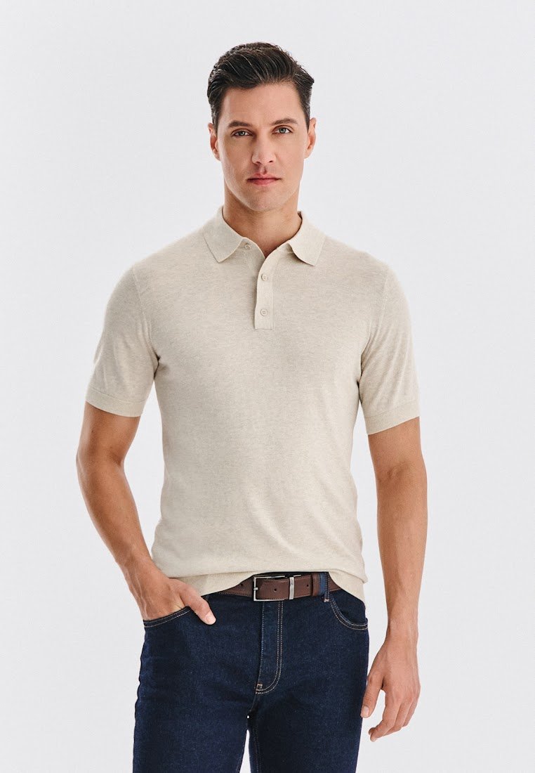 Beżowa koszulka polo z krótkim rękawem, z trzema guzikami, gładką fakturą i klasycznym kołnierzykiem, zestawiona z ciemnoniebieskimi dżinsami i brązowym paskiem.