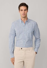 Lichtblauw gestreept overhemd met lange mouwen, een kraag en een borstzak, gecombineerd met beige broek.