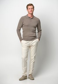 Hellebraunes Strick-Polohemd mit Kragen und einer Knopfleiste mit drei Knöpfen, kombiniert mit cremefarbenen Hosen und beigen Sneakers.