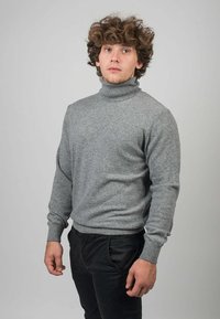 Grå polotröja i mjukt, texturerat tyg. Har långa ärmar och ribbade muddar, i kombination med mörka byxor.