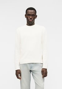 Κρεμ πουλόβερ με στρογγυλή λαιμόκοψη και ριμπ μανσέτες, συνδυασμένο με ανοιχτόχρωμο τζιν. Μαλακή υφή και άνετη εφαρμογή.