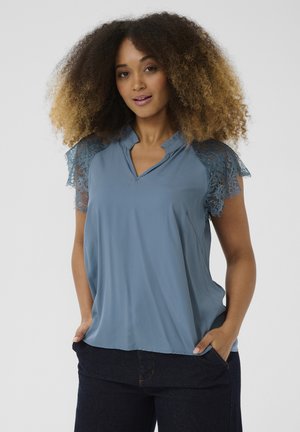 Lichtblauwe blouse met kanten cap mouwen en een V-hals. Zachte stof, ontspannen pasvorm, subtiele glans en zijkanten met zakken.