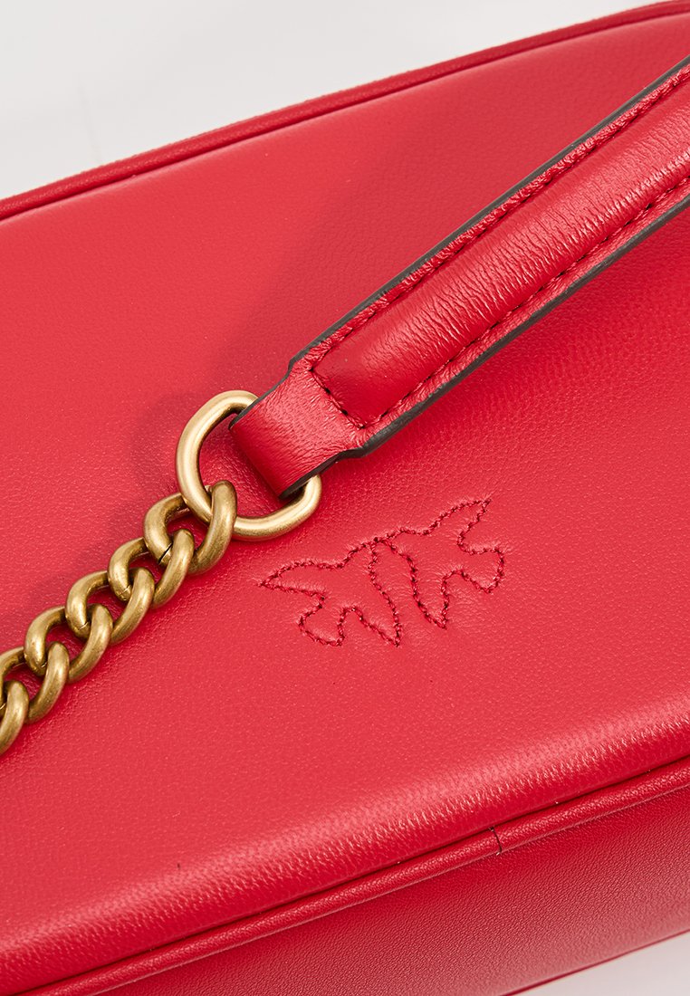 Sac en cuir rouge avec une chaîne dorée, présentant des détails embossés. Texture lisse et forme rectangulaire avec des bords contrastés.