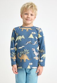 Sininen pitkähihaine ärsyttävän paidan jossa on dinosaurusten ja tulivuorten painatus vaaleissa väreissä. Kankaan on pehmeä, ribatoitu rakenne ja mukava istuvuus.