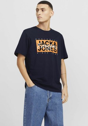 Navy blue cotton t-shirt featuring white and orange graphic text, round neck, short sleeves, and relaxed fit, paired with light blue jeans.