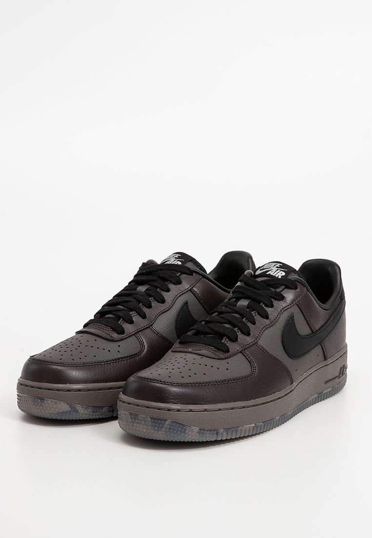 Par de zapatillas Nike Air en marrón oscuro y negro con cordones negros y suelas translúcidas grises sobre un fondo blanco.