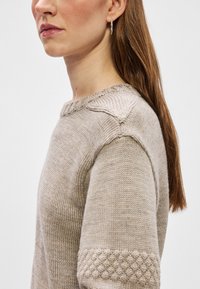 Beige knitted sweater with a ribbed round neckline, textured shoulder detail, and patterned accents on the sleeves. Smooth fabric.