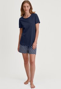 Marineblauwe katoen t-shirt met korte mouwen, gecombineerd met marineblauwe shorts met witte stippen. Zacht materiaal, casual pasvorm en ronde halslijn.