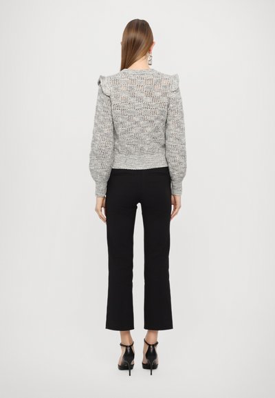 Pull en tricot gris avec des épaules volantes, motif texturé et ourlet côtelé, assorti à un pantalon noir et des talons noirs. Vue de dos visible.