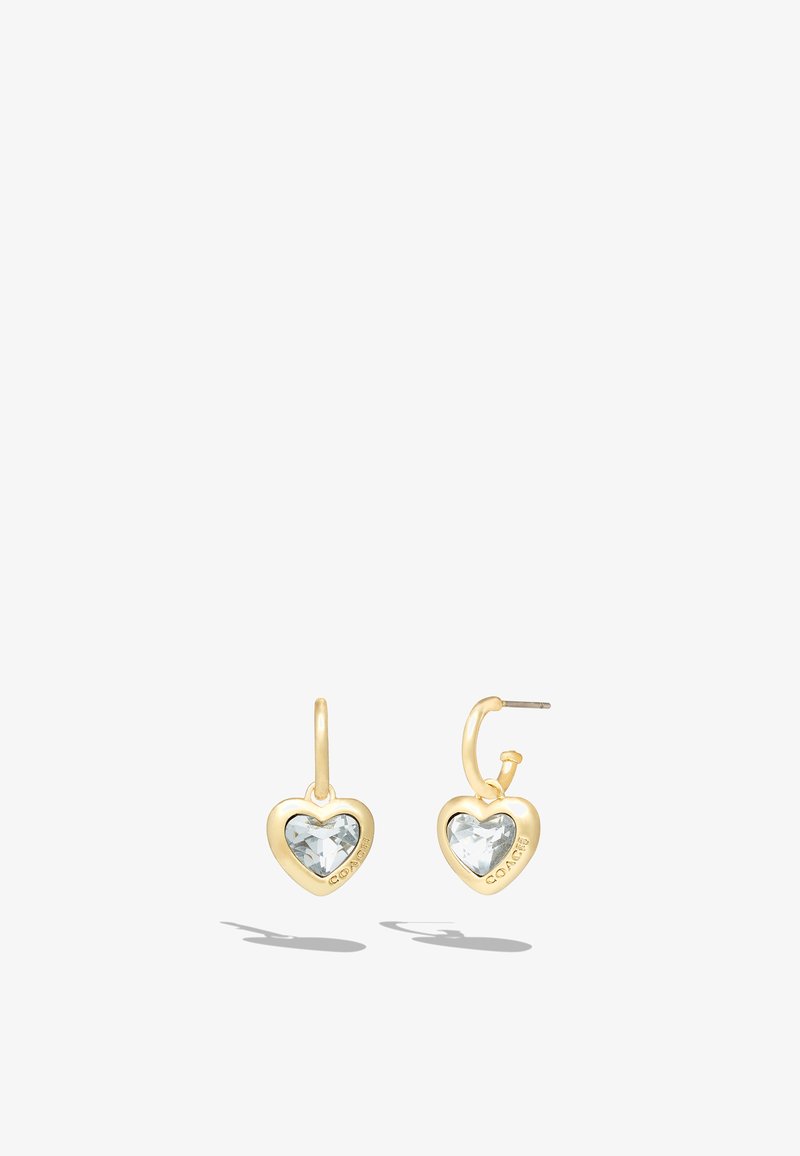 Gold-tone heart-shaped earrings featuring a faceted clear crystal center and a hook closure. Branding visible on the side.