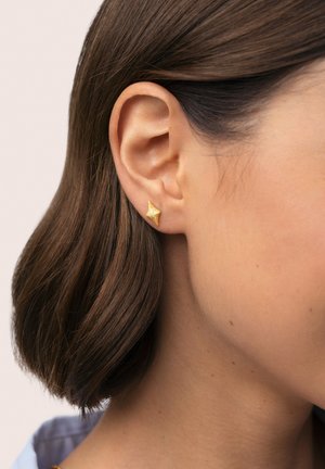Pendientes de botón de oro con forma de estrella texturizada, mostrados en una oreja parcialmente visible, destacando su brillo y diseño único.