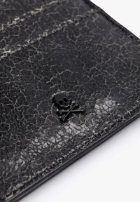 Billetera de cuero negro texturizado con una superficie agrietada y un pequeño logotipo de calavera y huesos cruzados en negro como acento decorativo.