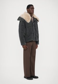 Tumehallist nööbiga jope, millel on beež kunstkarusnahk krae, lukuga kinnitamine, kaks eesmist taskut ja lõdva lõikega. Mudel kannab pruuni pükse.