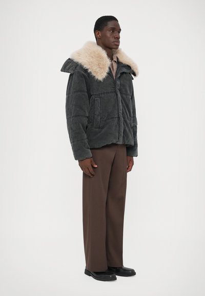 Mørkegrå kordjakke med en beige faux fur-krave, der har en lynlås lukning, to forlommer og en afslappet pasform. Modellen har brune bukser på.