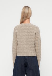 Beige, teksturert genser med stripete mønster og ribbestrikket kant, med lange ermer. Bakvinkelen viser en rund halslinje og mykt materiale.