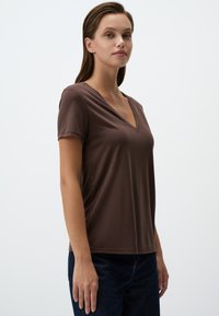 T-shirt marrone a maniche corte modello V, realizzata in tessuto morbido, aderente alle spalle e più larga all'orlo. Design semplice, senza fantasie.